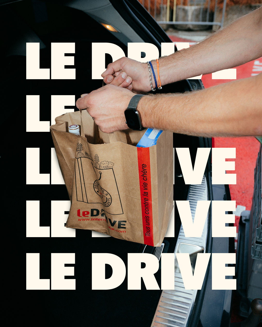 Un sac de courses Intermarché déposé dans le coffre, devant la typographie LE DRIVE.